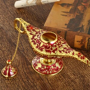 May include: A gold and red genie lamp with intricate floral designs and red jewels. The lamp has a chain attached to the spout and a small, matching lid.