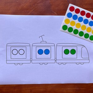 May include: A white paper with a black and white outline of a train with three cars. The train has two blue circles in the middle car, two white circles in the first car, and two green circles in the last car.