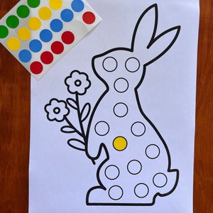K&ouml;nnte beinhalten: Eine schwarz-wei&szlig;e Umrandung eines Kaninchens, das eine Blume h&auml;lt. Das Kaninchen hat einen gelben Punkt auf der Brust und ist von wei&szlig;en Kreisen umgeben. Auf einem separaten Blatt Papier befinden sich rote, blaue, gelbe und gr&uuml;ne Kreise.