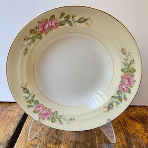 May include: A white soup bowl with a gold rim and a floral pattern of pink roses and green leaves.