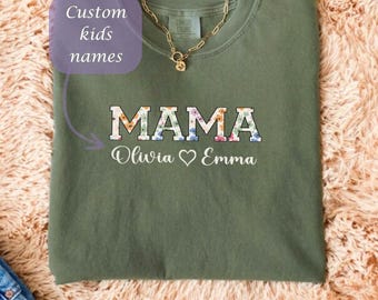 May include: Olive green t-shirt with the word "MAMA" in a floral design. Below the word "MAMA" are the names "Olivia" and "Emma" with a heart symbol between them. The text "Custom kids names" is also visible.