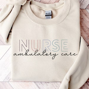May include: A beige sweatshirt with the text "NURSE ambulatory care" in colorful outlined letters. The text is in a modern font style.
