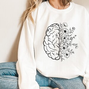 May include: White sweatshirt with a black and white graphic of a brain with flowers growing out of it.