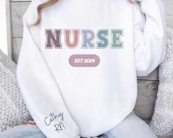 May include: White sweatshirt with the word "NURSE" in rainbow colors and the text "EST 2024" in a light pink oval. The sleeve has the text "Cathy RN" written in black.