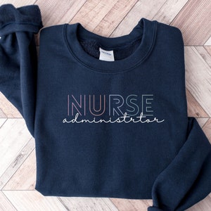 May include: A navy blue sweatshirt with the text "NURSE administrator" in a rainbow color gradient.