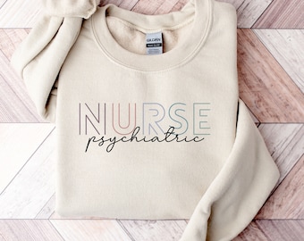 May include: A beige sweatshirt with the text "NURSE psychiatric" in a colorful, layered font.