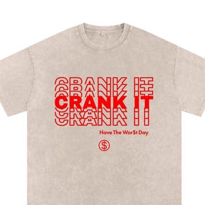 May include: A beige short-sleeve t-shirt with a washed-out texture. The front features red text that reads CRANK IT in a layered, repeating style, followed by the text Have The Wor$t Day and a circular symbol containing a dollar sign.