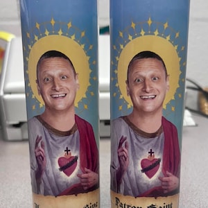 May include: Two glass prayer candles with a blue background and a portrait of a smiling man with a halo. One candle reads "You Gotta Give", the other reads "Patron Saint of Friendship".