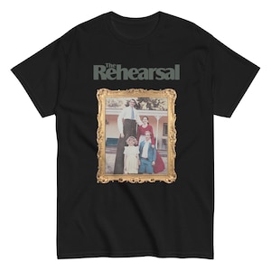 Pode incluir: Camiseta preta com o texto "The Rehearsal" acima de uma imagem emoldurada de uma família. A imagem emoldurada tem uma borda dourada e retrata um homem, uma mulher e duas crianças. O homem está em pernas de pau.