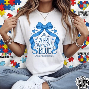 Puede incluir: Camiseta blanca con un diseño de lazo azul y el texto "IN APRIL WE WEAR BLUE". La camiseta también incluye las palabras "Accept, Understand, Love" y está rodeada de corazones. La camiseta promueve la concienciación sobre el autismo.