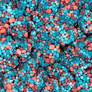 May include: Close-up of a pile of colorful candies. The candies are a mix of small, round pieces in shades of blue, coral, and brown. The texture appears to be slightly bumpy, and the overall effect is visually appealing.