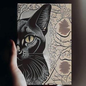 May include: A black and white illustration of a cat's face with a yellow eye. The background is cream coloured with a black and white floral pattern.