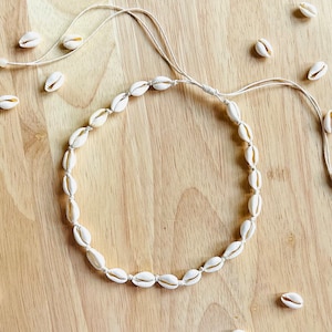 May include: A white shell necklace with a simple design. The necklace is made of small, white shells strung together on a white cord.
