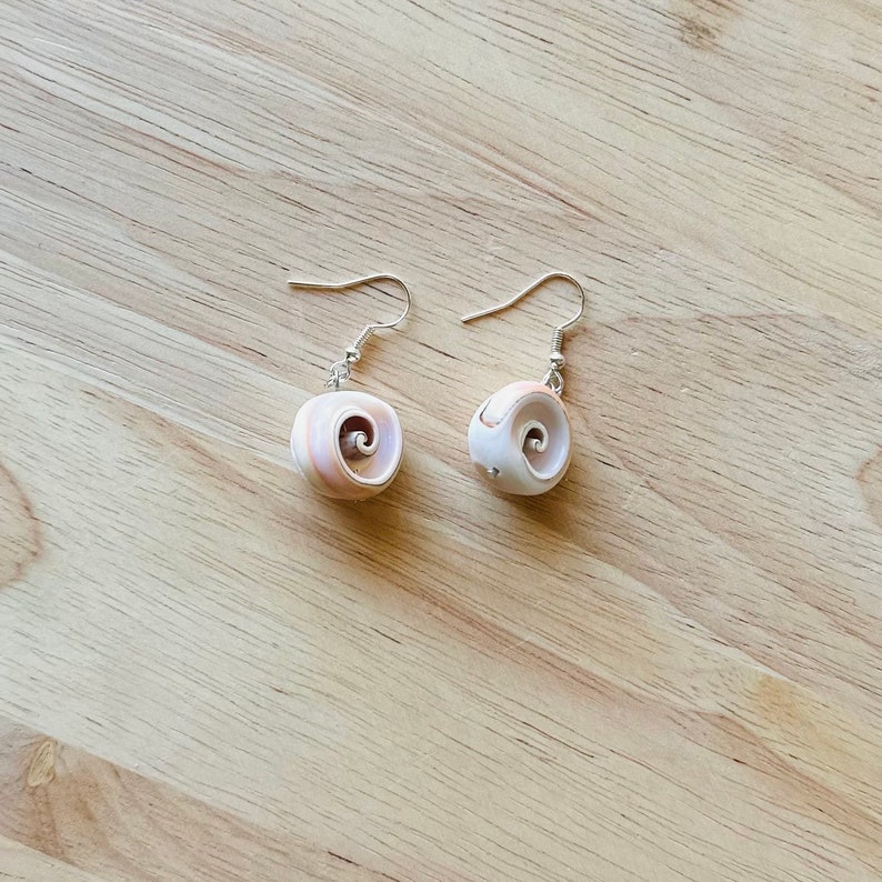 May include: A pair of silver earrings with a white and pink seashell design.