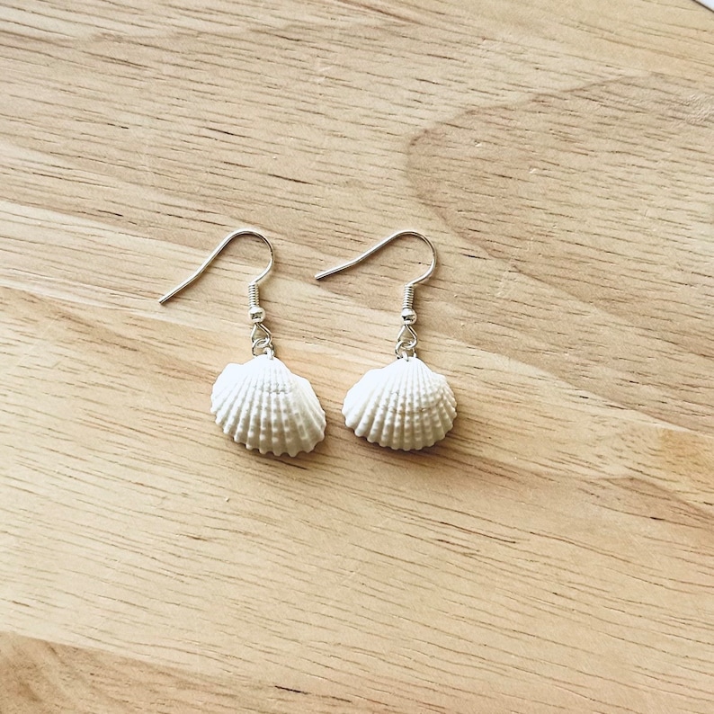 May include: A pair of white seashell earrings with silver hooks. The earrings are small and delicate, and they would be perfect for a summery look.
