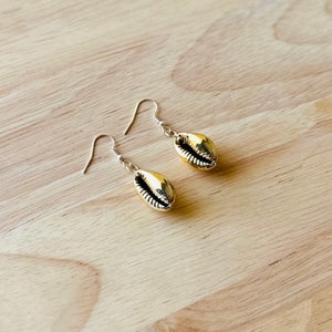 May include: A pair of gold-tone shell earrings with silver hooks. The earrings are shaped like a cowrie shell.