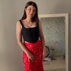 May include: A woman wearing a black corset top with a red floral skirt. The skirt has a white floral pattern.