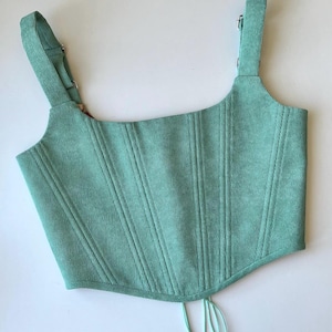 May include: A mint green corduroy corset top with adjustable straps and a lace-up back.
