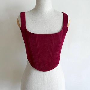 Puede incluir: Un top de corsé de color burdeos con textura de canalé, escote cuadrado y tirantes finos.