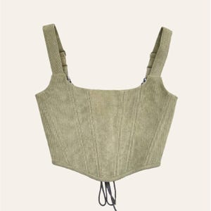 May include: A sage green corset top with adjustable straps and a square neckline. The structured bodice has vertical seam detailing and a lace-up closure. The straps are attached with metal hardware.
