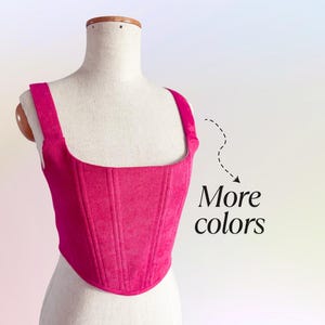 May include: A vibrant fuchsia corset top with a square neckline and wide straps, displayed on a mannequin. The corduroy fabric features vertical ribbing. Text on the right says "More colors".