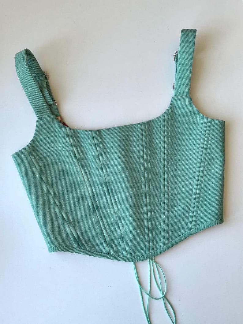 May include: A mint green corduroy corset top with adjustable straps and a lace-up back.
