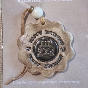 May include: A ceramic essential oil diffuser shaped like a flower with the words "Happy Birthday" and a cake with candles in the centre. The diffuser is beige with gold accents.