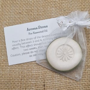 May include: Aroma stone for essential oil, packaged in a sheer white organza bag with a ribbon. The round, off-white stone features a floral design. A white card with instructions is included.