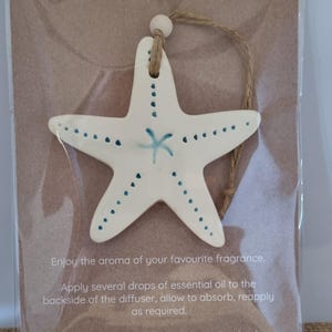 May include: A white ceramic starfish with blue dots and a blue starfish design in the centre. The starfish is hanging from a string and is packaged on a brown card with the text "Essential Oil Diffuser" and instructions for use.