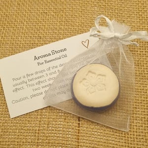 May include: An aroma stone for essential oil, in a sheer white organza bag. The round, off-white stone has a floral design. A card with instructions is included, with the text "Aroma Stone For Essential Oil".