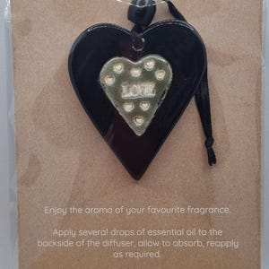 May include: Black heart-shaped essential oil diffuser with a central heart design and the word "LOVE". It hangs from a black ribbon and is presented on a brown card with instructions for use.
