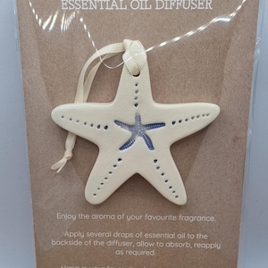 May include: Cream ceramic starfish essential oil diffuser with a blue starfish design. It has a ribbon for hanging and the text "ESSENTIAL OIL DIFFUSER". Instructions are also printed on the card.