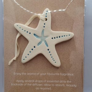 May include: Cream ceramic starfish essential oil diffuser with blue detailing. The starfish is strung with a cream ribbon and is displayed on a brown card. The card reads "ESSENTIAL OIL DIFFUSER".