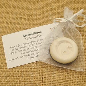 May include: Aroma stone for essential oil, in a sheer white organza bag. The off-white stone features a crescent moon and star design. A white card with instructions is included, set against a hessian background.
