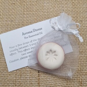 May include: Aroma Stone for essential oil, in a sheer white organza bag. The round, off-white stone has a floral design. A white card with instructions is visible. Ideal for aromatherapy.