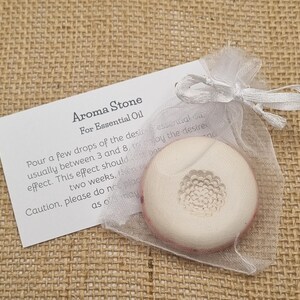 May include: Aroma stone for essential oil, in a sheer white organza bag. The round stone has a floral design and a pink border. A white card with instructions is included.
