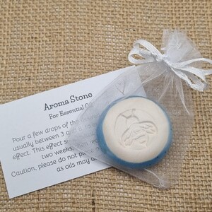 May include: Aroma stone for essential oils, in a sheer white organza bag. The round stone has a white top, blue rim, and a bee design. A card with instructions is included. Ideal for aromatherapy.