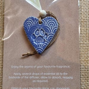 May include: A blue ceramic heart-shaped essential oil diffuser with a paw print design. The diffuser has a string attached to it and is packaged on a brown card with instructions for use. "ESSENTIAL OIL DIFFUSER" is printed at the top of the card. "Enjoy the aroma of your favourite fragrance. Apply several drops of essential oil to the backside of the diffuser, allow to absorb, reapply as required. Hang in your favourite place, car, doorknob, wardrobe or office."