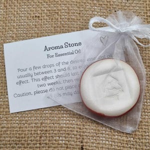 May include: Aroma stone for essential oil, in a sheer white organza bag with a drawstring. The round, white stone has a tree design and a red edge. A card with instructions is included. Ideal for aromatherapy.