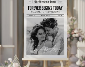 May include: A wedding sign displayed on a wooden easel. The sign is designed to look like a newspaper front page, with the headline "FOREVER BEGINS TODAY." It includes a black and white photo of a couple and the names "Ezekiel & Angela."