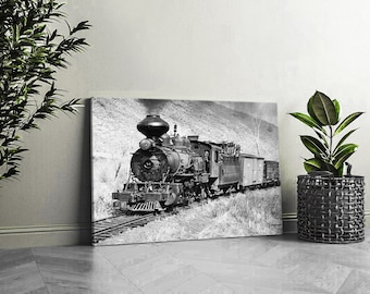 May include: Black and white photograph of a vintage steam locomotive train engine pulling a line of boxcars. The train is on a track in a rural setting.