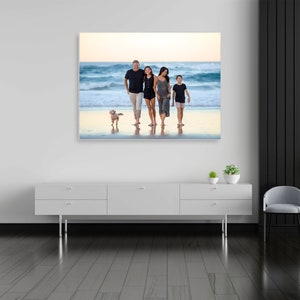 May include: A family of four walks along a sandy beach with their dog. The family is wearing casual clothing and smiling. The beach is empty and the water is blue. The sky is a light blue with some clouds.
