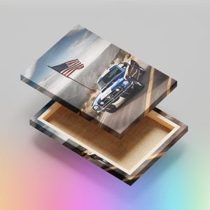 May include: A blue Ford Mustang sports car driving on a road with a waving American flag in the background. The car is on a canvas print with a wooden frame.