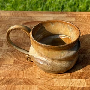 May include: A handmade ceramic mug with a unique, layered design. The mug features a wide, open top and a sturdy handle. The color is a warm, earthy brown with subtle variations, suggesting a natural, organic aesthetic. The mug is likely used for drinking beverages.