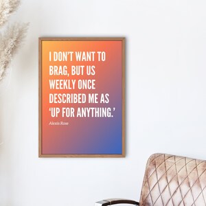 May include: A framed print with a gradient background of orange, yellow, and purple. The print features a quote by Alexis Rose: "I don't want to brag, but us weekly once described me as 'up for anything.'"