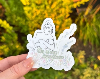 May include: A white sticker featuring a line drawing of a person breastfeeding a baby, with floral embellishments. The sticker includes the text "this is my superpower" in a script font.