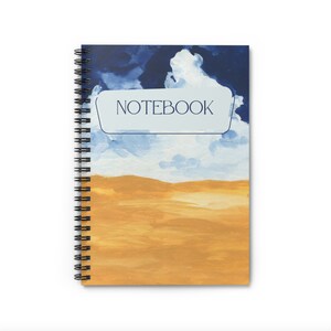 Pode incluir: Um caderno espiral com um design de aquarela azul e amarelo. A capa apresenta um céu azul com nuvens brancas e um campo amarelo. A palavra "NOTEBOOK" está impressa em um retângulo branco na capa.