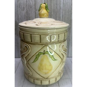 May include: A ceramic canister with a cream and tan finish, featuring a raised diamond pattern and a painted yellow pear motif. The lid is topped with a sculpted yellow pear handle, and the body is decorated with embossed scrollwork details.