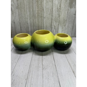 May include: A three-section ceramic planter with a rounded shape. The planter is yellow at the top, transitioning to a dark green at the base. The interior of each section is yellow.