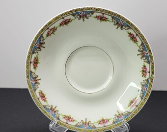 May include: A white porcelain saucer with a gold rim and a floral design in shades of pink, blue, and green. The design features a repeating pattern of roses and stylized leaves.